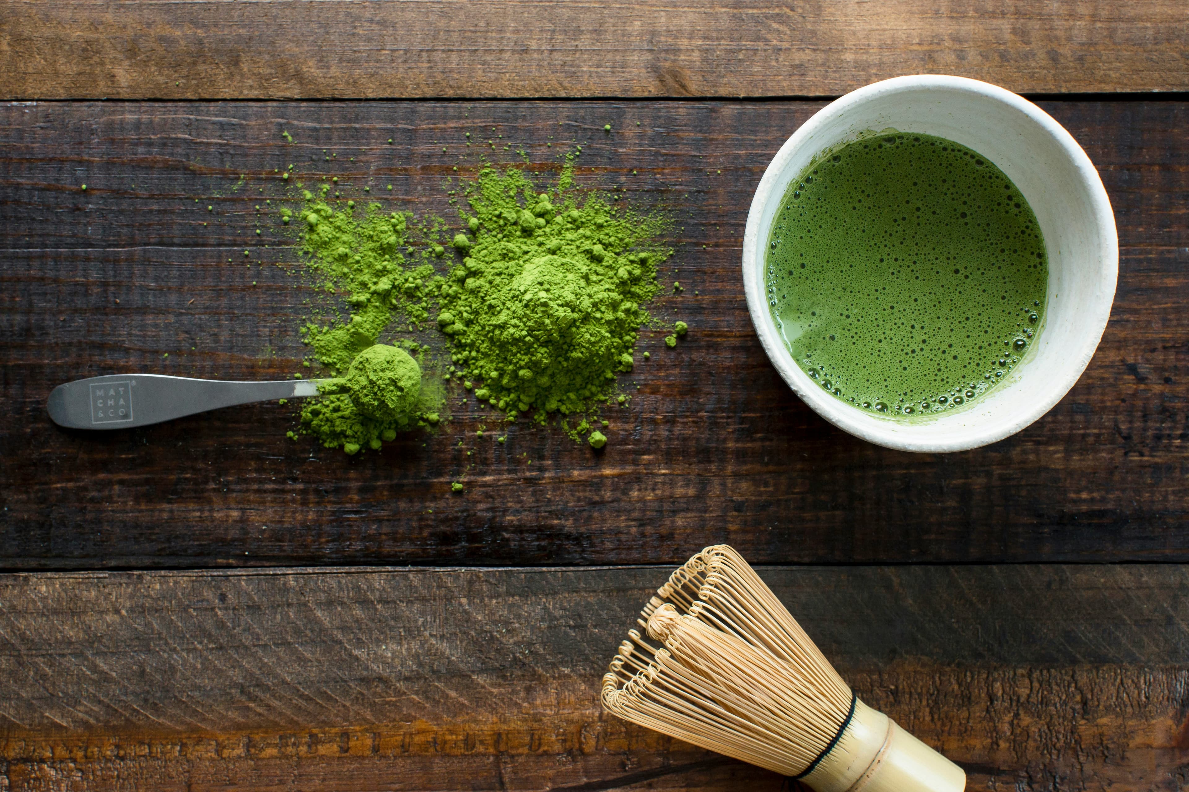Fresh matcha powder with bowl and bamboo whisk on dark wood
